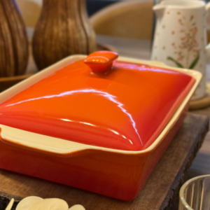 Caçarola cerâmica da cor laranja em uma mesa posta, mostrando ao fundo uma garrafa da linha Valentina