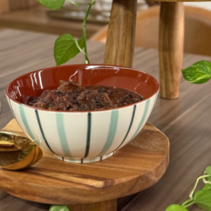 Tigela Marrom de Cerâmica com Listras em seu exterior alternando entre azul e verde, servindo uma feijoada em uma mesa posta.